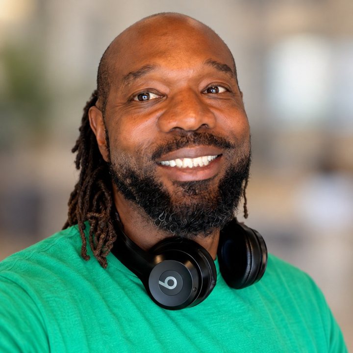Masada M.E. Ellis, President and Executive Director, smiling in a green shirt with headphones resting around his neck.