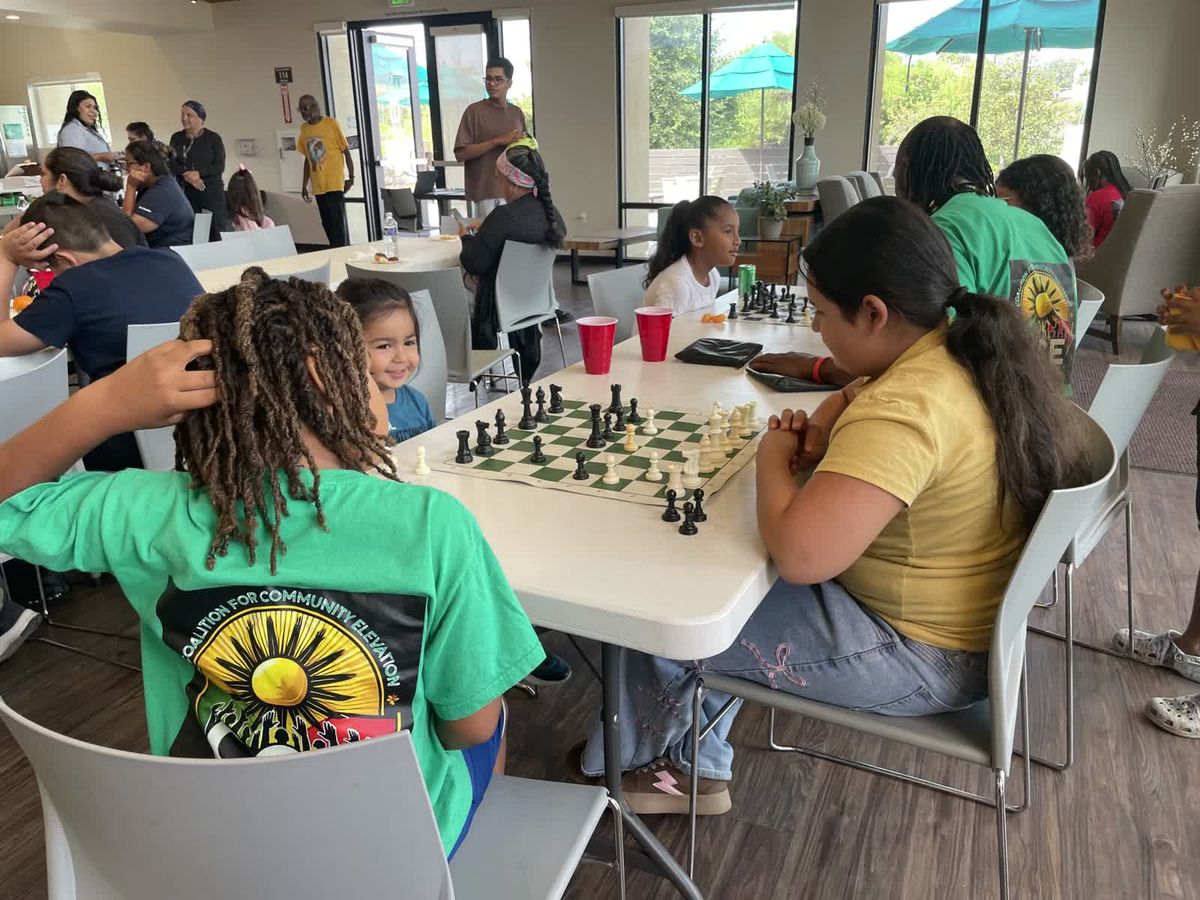 Young people leaning over chess boards at a table during a CCE student event.