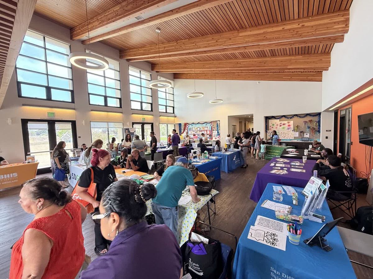 Neighbors browsing resource tables staffed by local organizations inside a community hall.